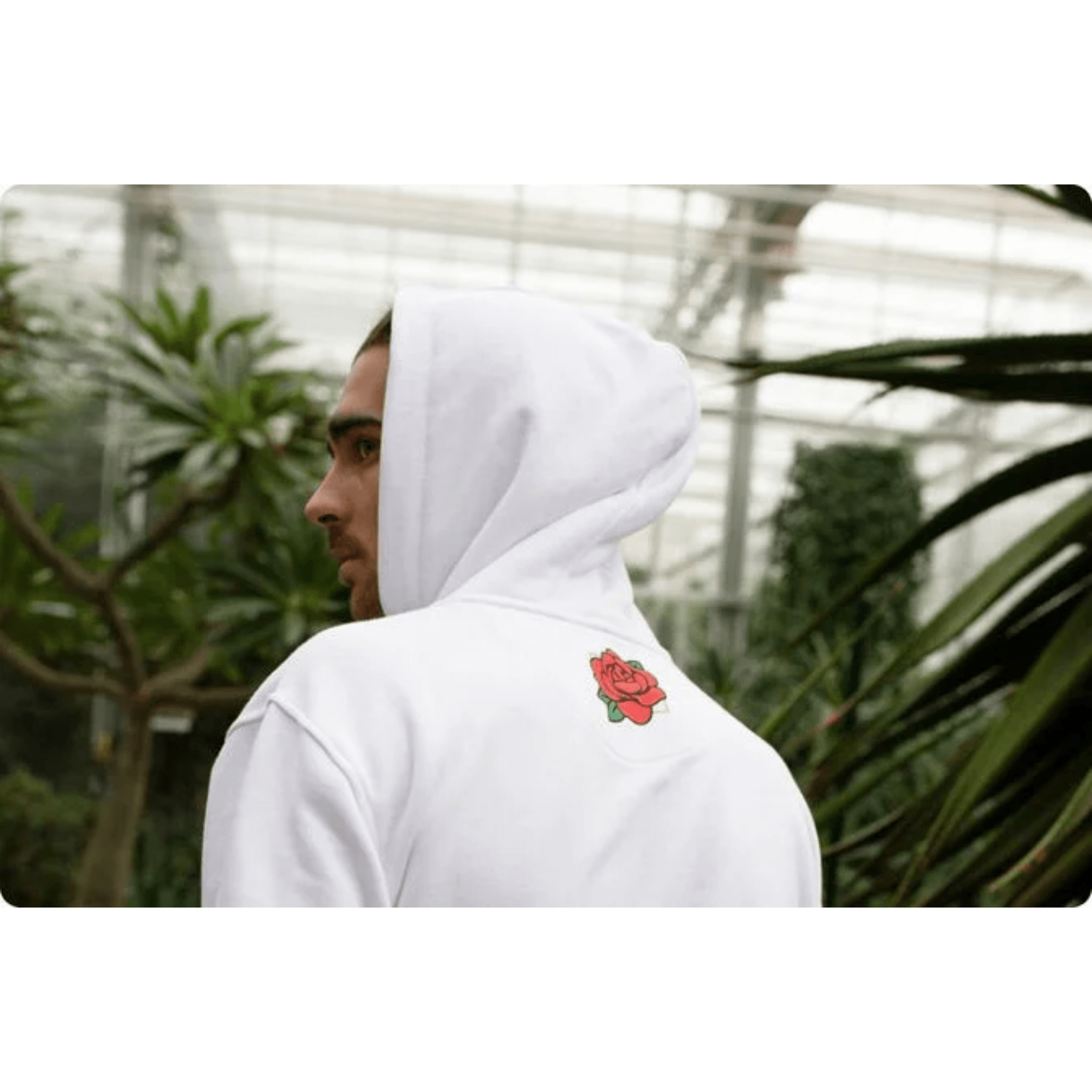 Person wearing a white hoodie with a red rose design in a greenhouse setting