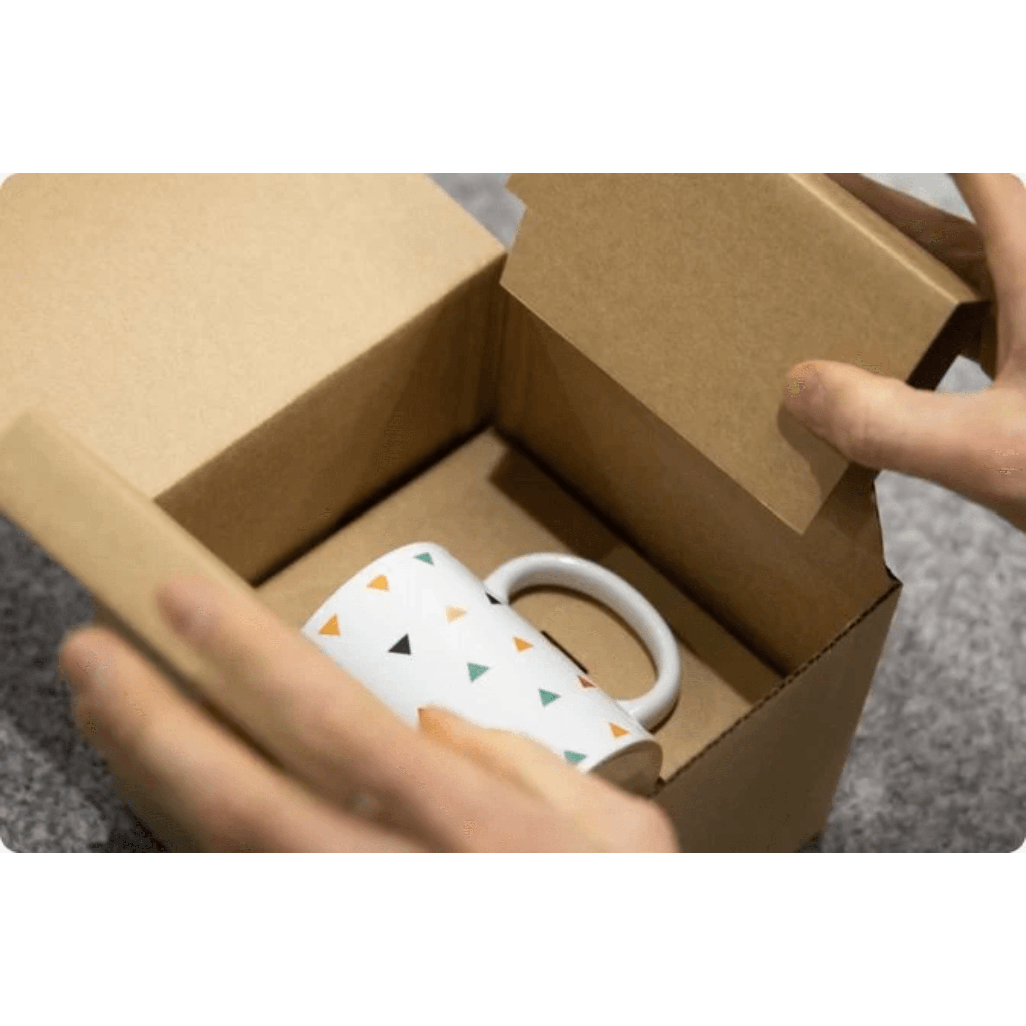 White mug with colorful triangle pattern inside an open cardboard box, held by a hand.